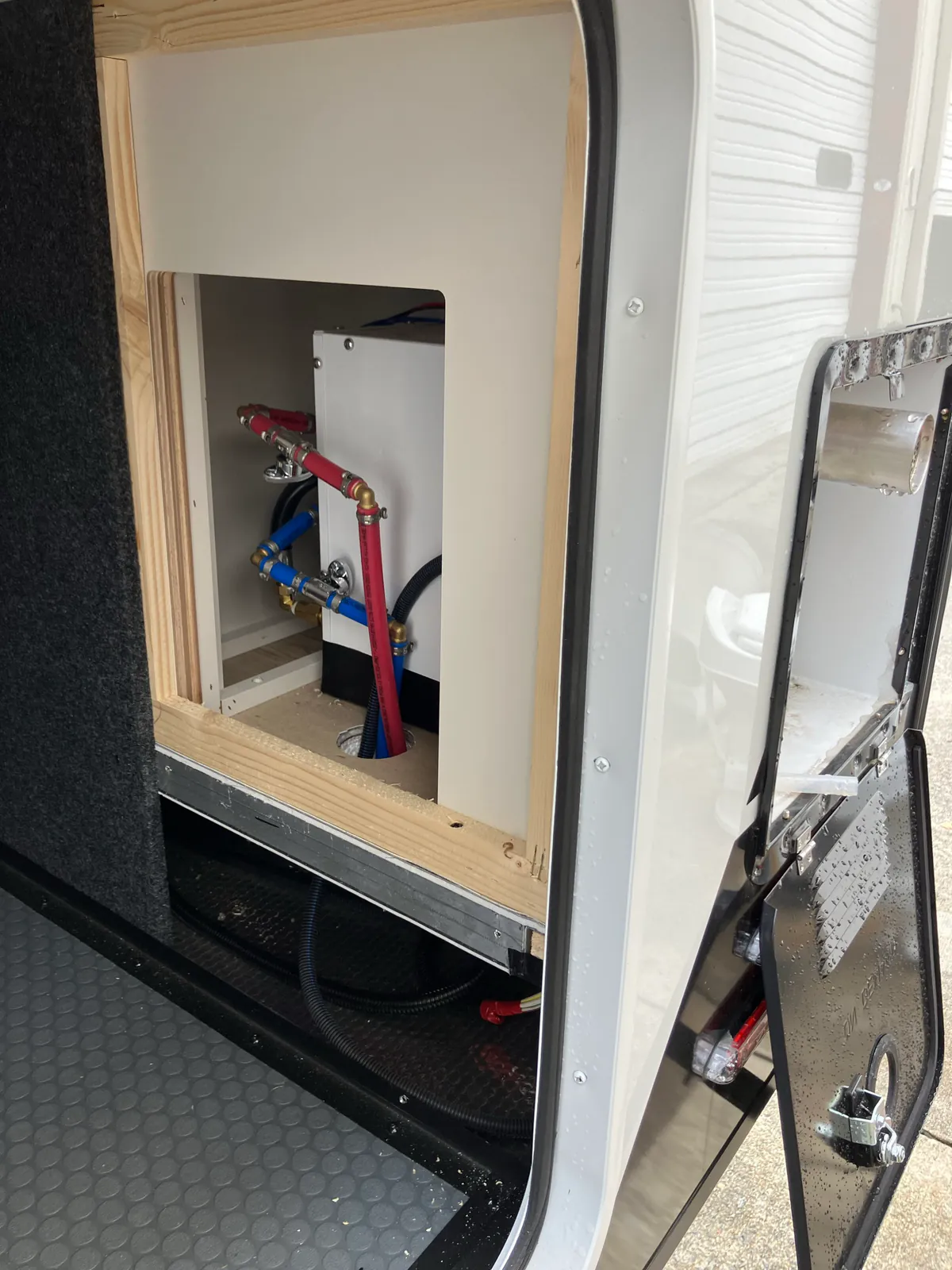Rear access opening beside a Brinkley Model Z tankless water heater showing plumbing and wiring