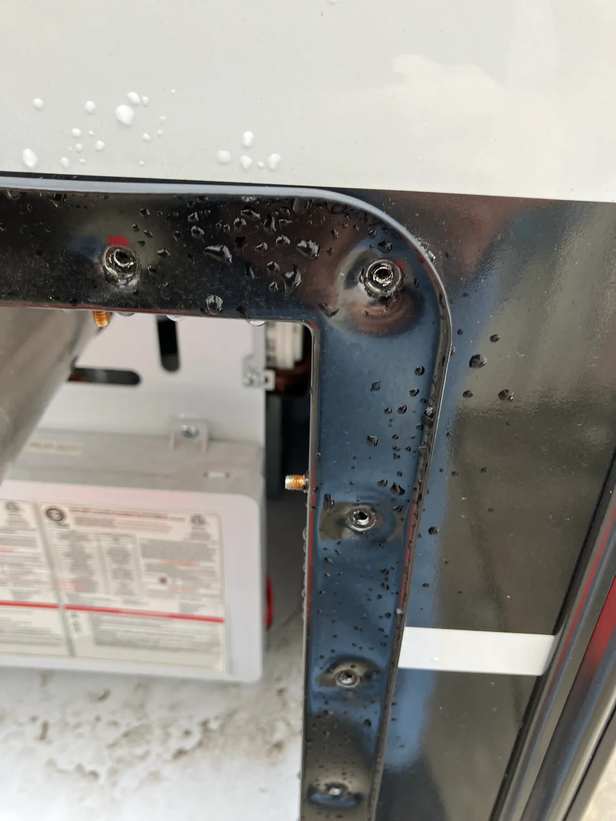Exterior mounting screws removed from the black flange of a Brinkley tankless water heater