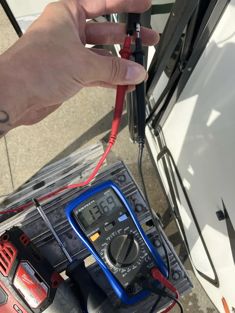 Digital multimeter measuring 13.69 volts DC across an unplugged RV awning motor connector