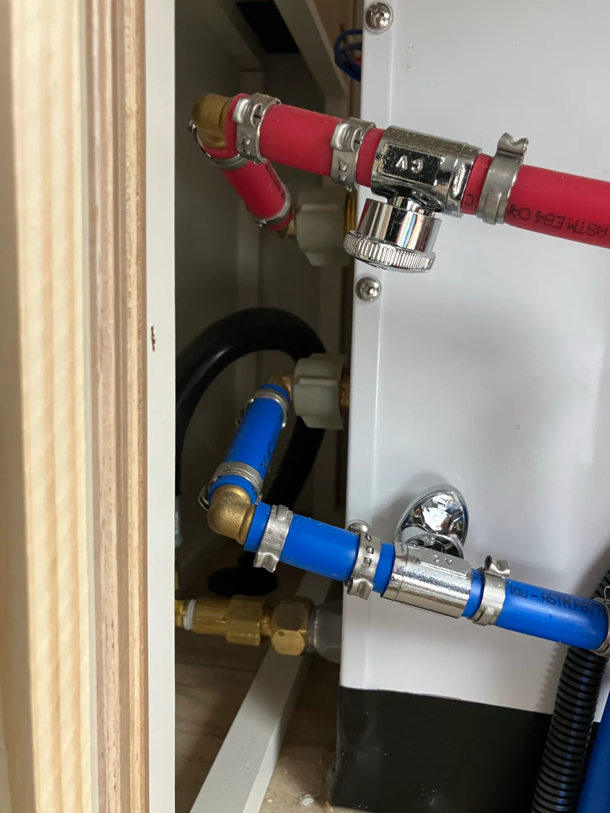 Red hot-water and blue cold-water PEX connections behind an RV tankless water heater