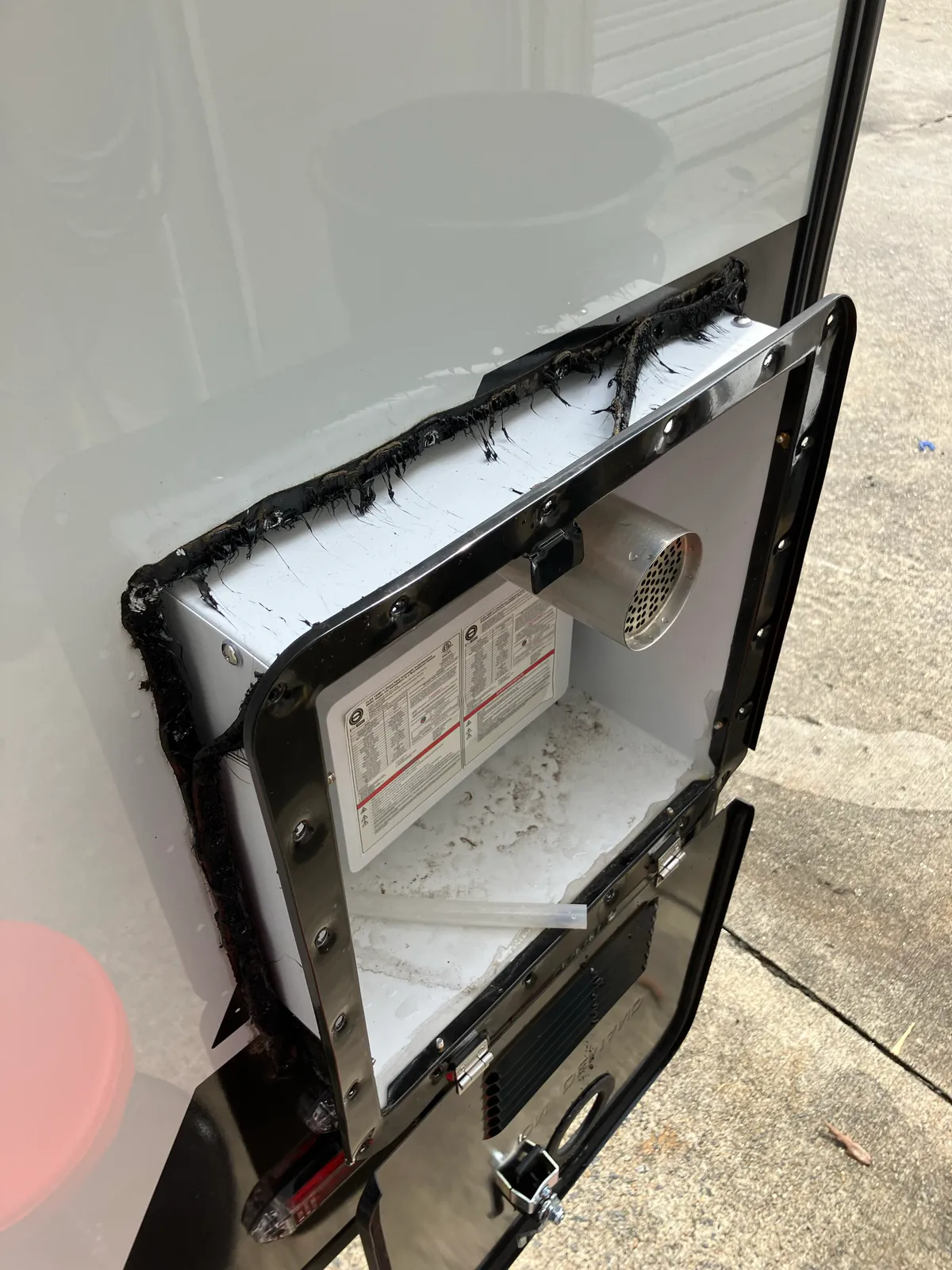RVMP Flex Temp tankless water heater partly removed from an RV sidewall with old black sealing material around the flange